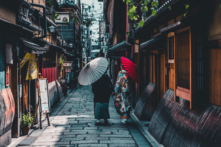Two women walking with umbrellas on a brick street in Kyoto, Japan
