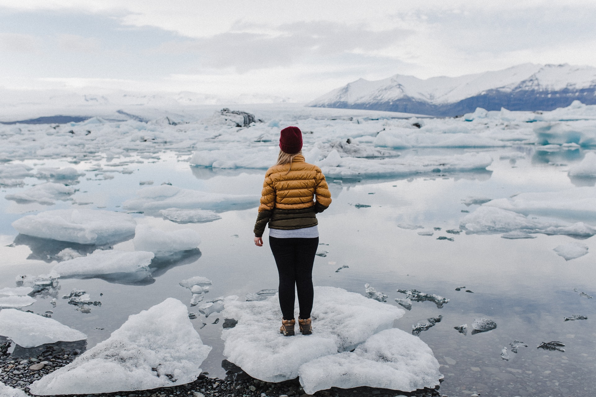 Woman standing on a block of ice in an Arctic location looking out over melting glaciers.