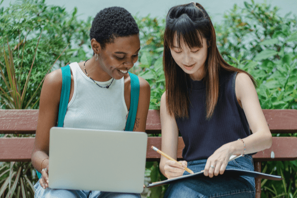 Two women studying together on a bench