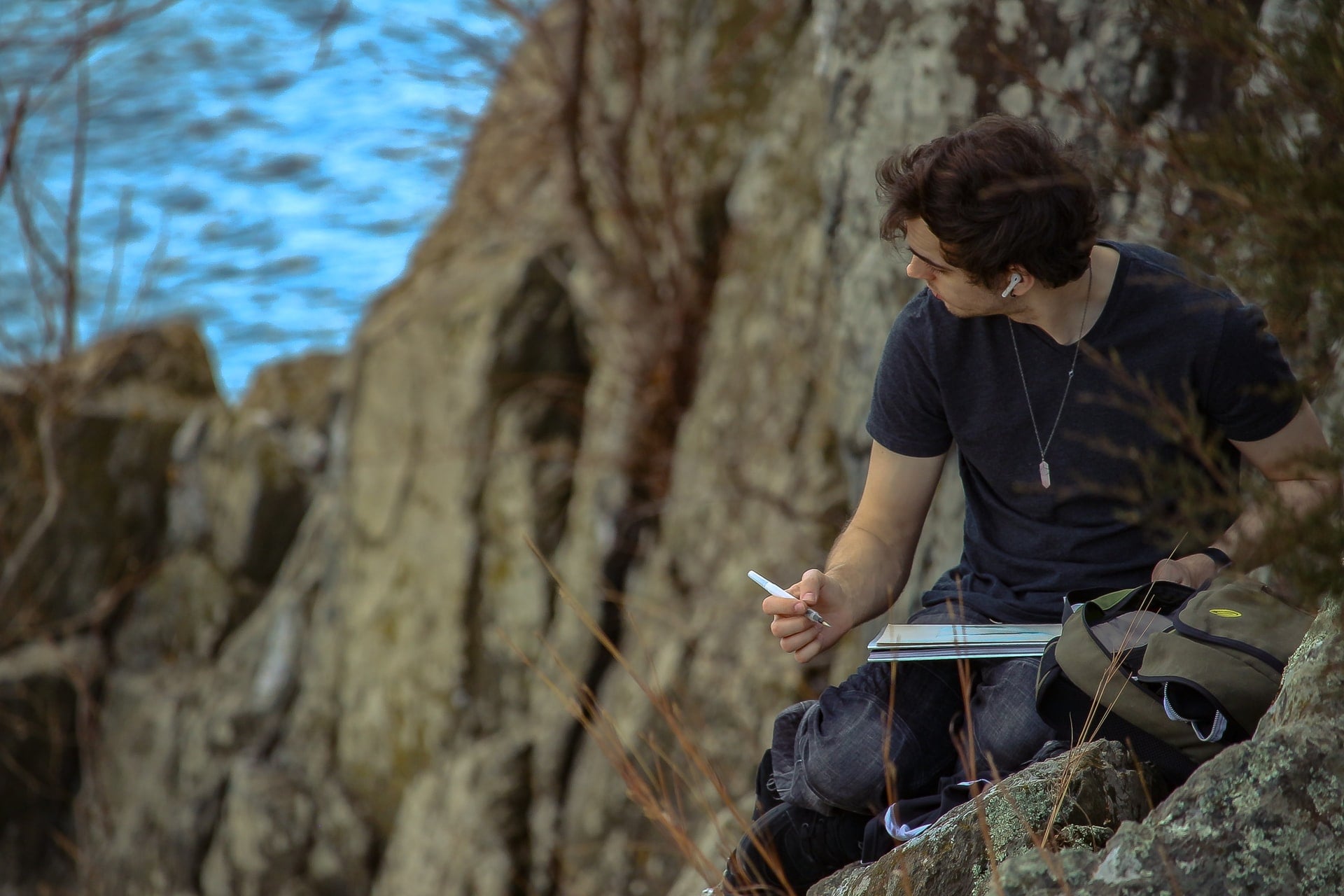 A man perched on a rocky mountainside writing