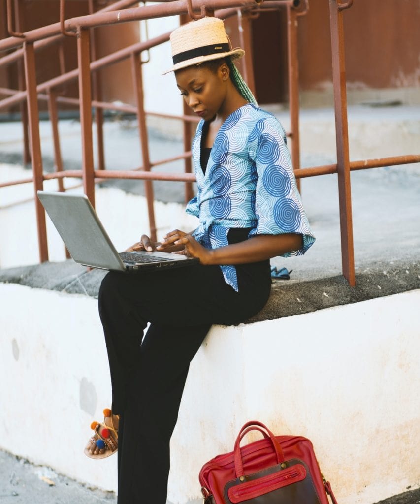 A Black travel blogger sitting outside and working on a laptop