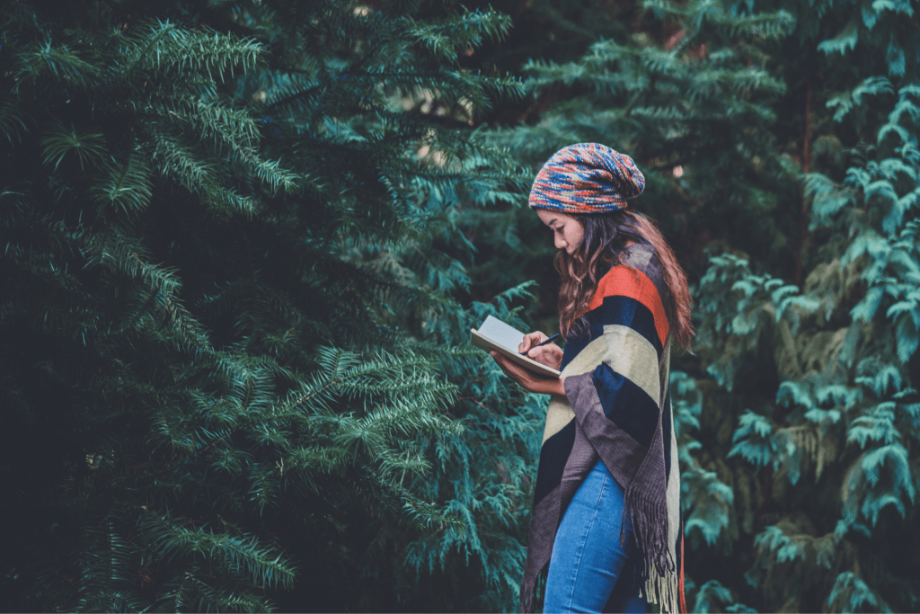 Woman standing in lush green forest writing in a notebook